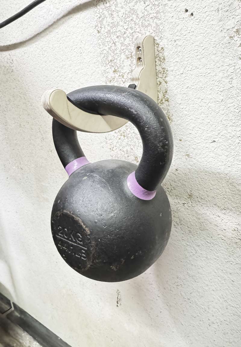 Single wooden snowboard rack shown holding a black 44 pound kettle bell demonstrating the strength of the rack while it is mounted to the wall. 