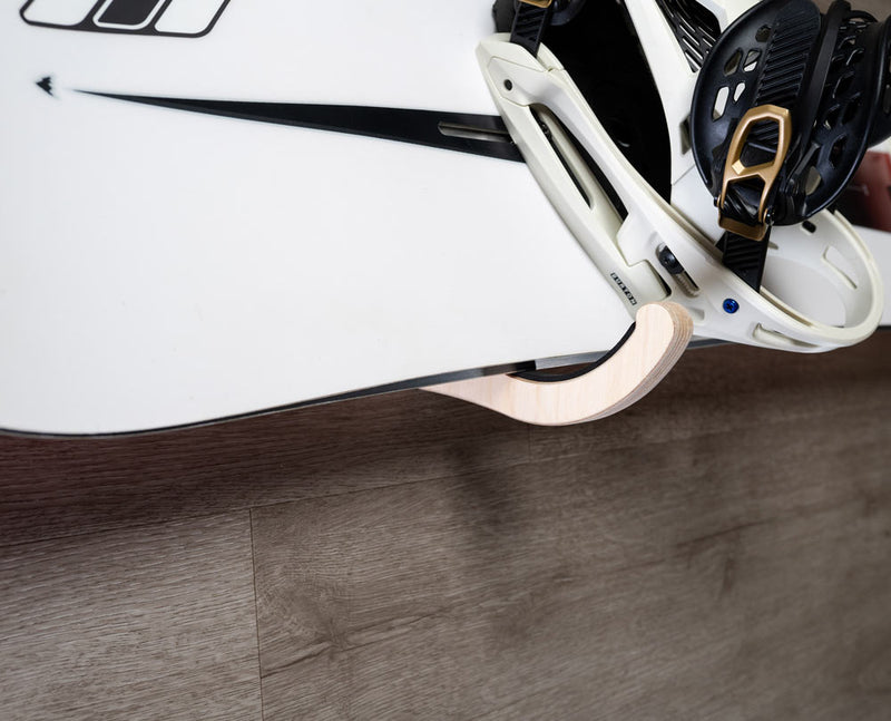 Side angle of the single wooden snowboard rack holding a white snowboard with white and black bindings.