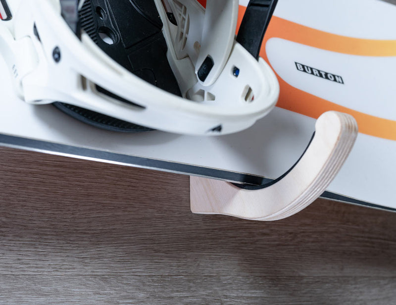 Close up of wooden snowboard rack showing how the board's edges are protected by the rack's foam padding.