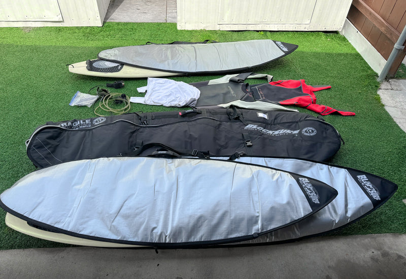 Various surfboard day bags shown on faux grass with other surfing travel gear next to them. 