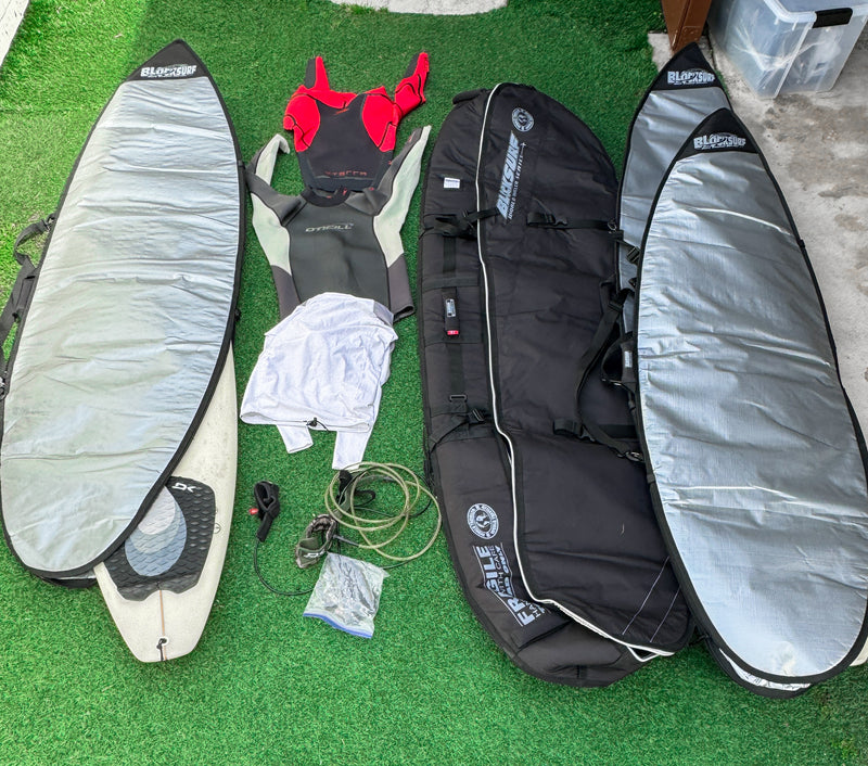 Several surfboard bags laid out on fake grass with some other surfing essentials such as wetsuits and leashes