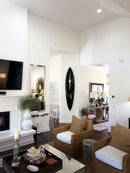 Black surfboard vertically mounted in aModern living room with brown furniture, white walls, and decorative elements.