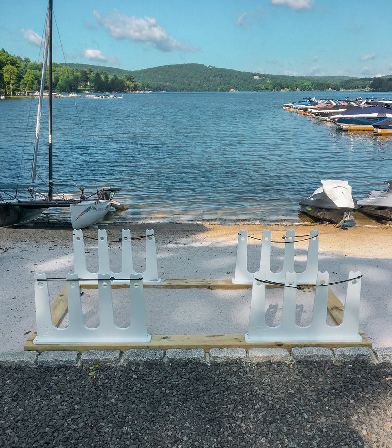 White dock racks built into the beach at a lake.  There are tree covered mountains in the background past the lake. 