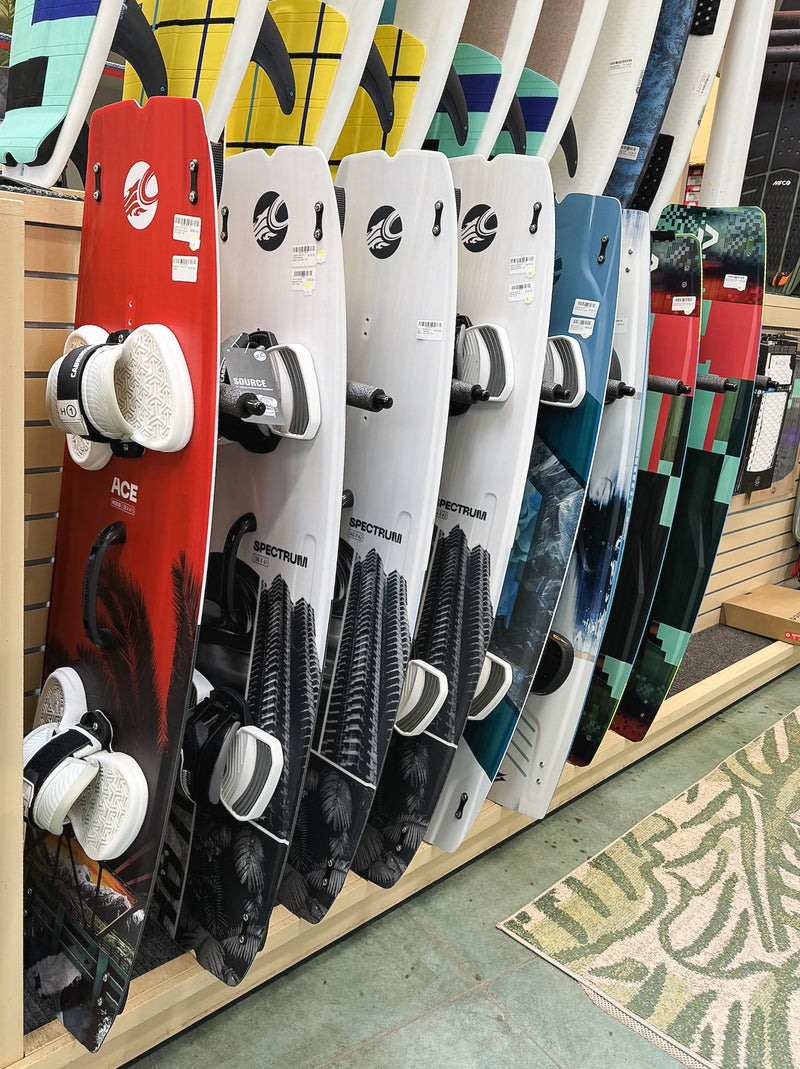Wake surf and Kite surf boards mounted vertically in a surf shop.  The boards have bindings / foot straps attached to the boards.