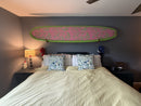 Wood Wall Rack above bed, holding green and pink surfboard. 