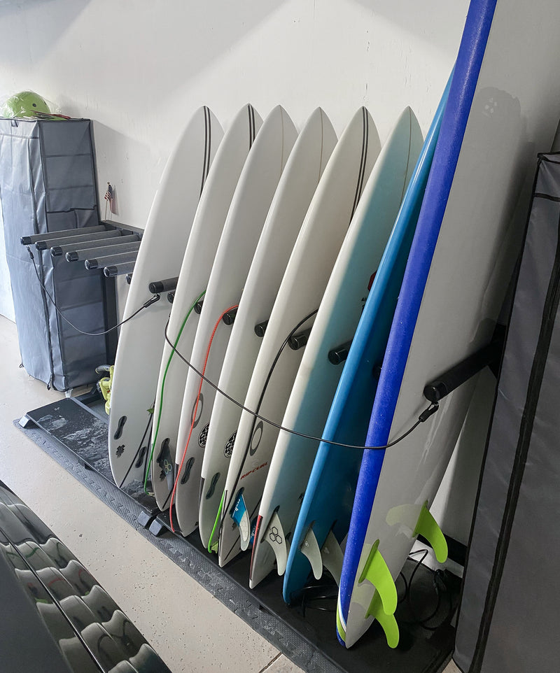 Blackout foamy surf racks displaying several shortboards and a soft-top longboard. The flat-black rack appears to be in a customers garage.