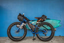 Blue Mountain bike with a surf rack attached holding 2 shortboards, and a bunch of gear ready to go camping and surfing.
