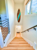 Wooden staircase with a surfboard art piece on the wall, leading to a bright room with large windows.