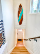 Wooden surfboard with blue accent hanging on a white wall above a staircase.
