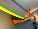 Wooden wall hook holding a green surfboard against a neutral wall.