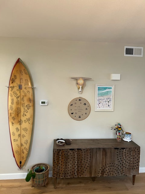 Acrylic shortboard rack shown hanging a collectors board in a living space with wooden floors, white trip and brown furniture