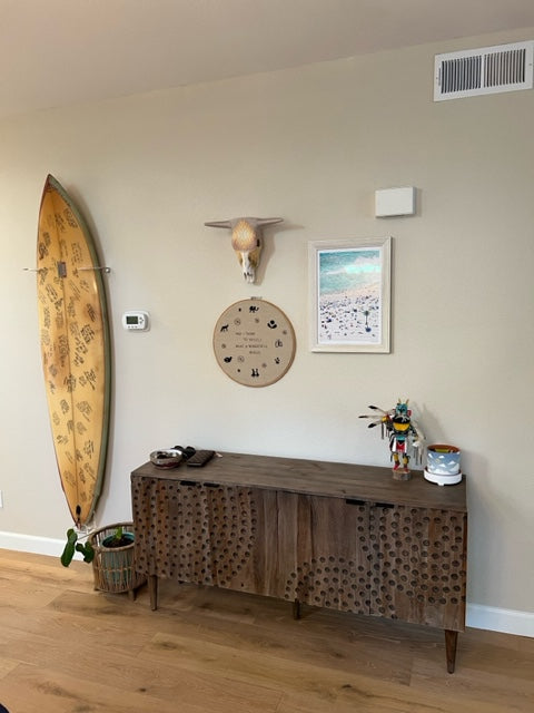 acrylic shortboard vertical wall rack shown holding a yellow surfboard in a living space with brown furniture and beach vibes