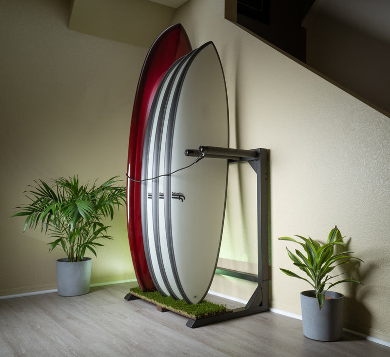 Blackout grassy surfboard rack shown displaying several surfboards in a clean home.  Next to plants with a green dramatic light. 