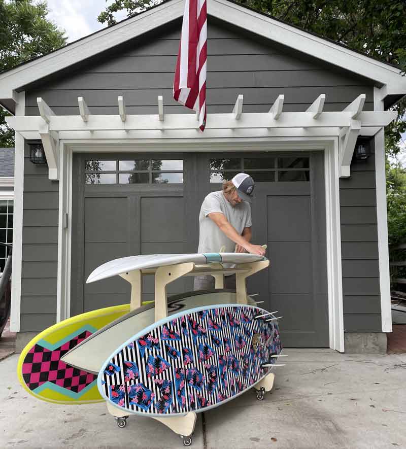 Epic board horse being used in a back yard in front of a garage.  Someone is Putting fins in.  There are several boards in the rack. 