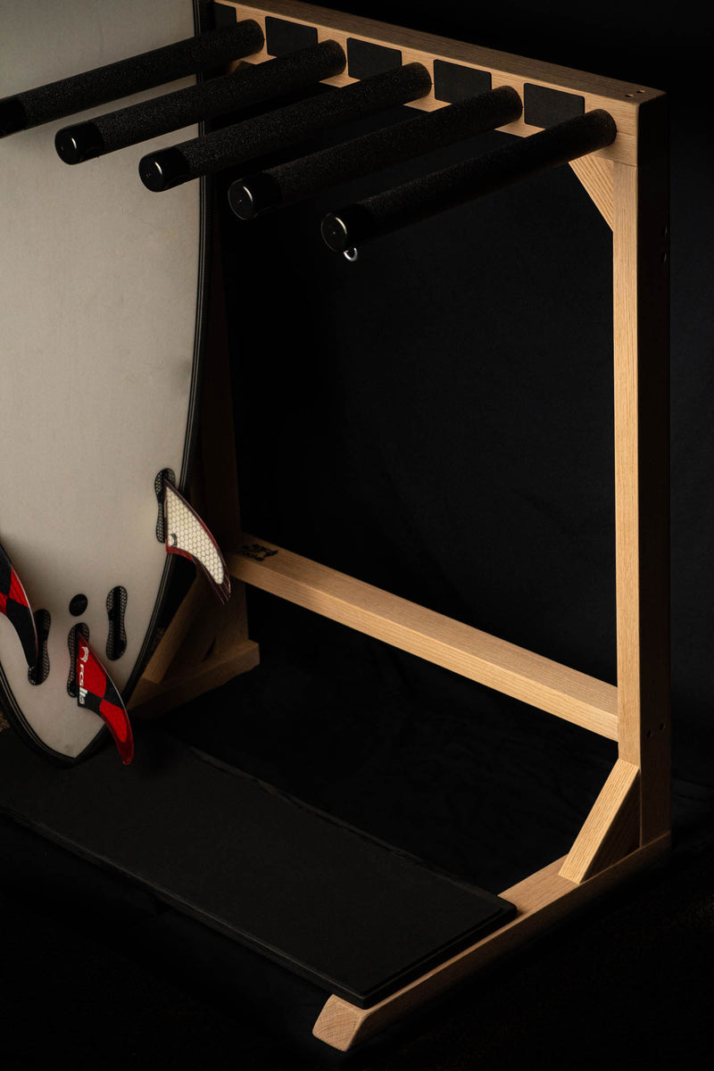 Red Oak Foamy Freestanding Surf Rack with black foam protective base for surfboards tail. Dramatic side lighting with a black backdrop. Single surfboard with Red fins.
