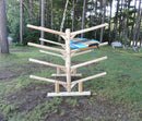 Side profile of the 8 boat freestanding log Kayak and SUP/Canoe rack.  Shown on the grass holding one Blue Stand Up Paddleboard, with Trees and lawn furniture in the background. 