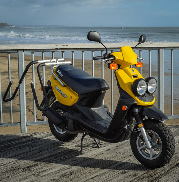 Dual-Mount moped rack shown mounted on a yellow moped by the beach.
