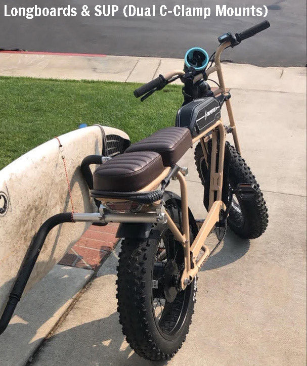 Beige electric Super 73 e-bike parked in a driveway with a surfboard rack mounted to the left holding a white performance surfboard.  White text reads Longboards & SUP (Dual C-Clamp Mounts)
