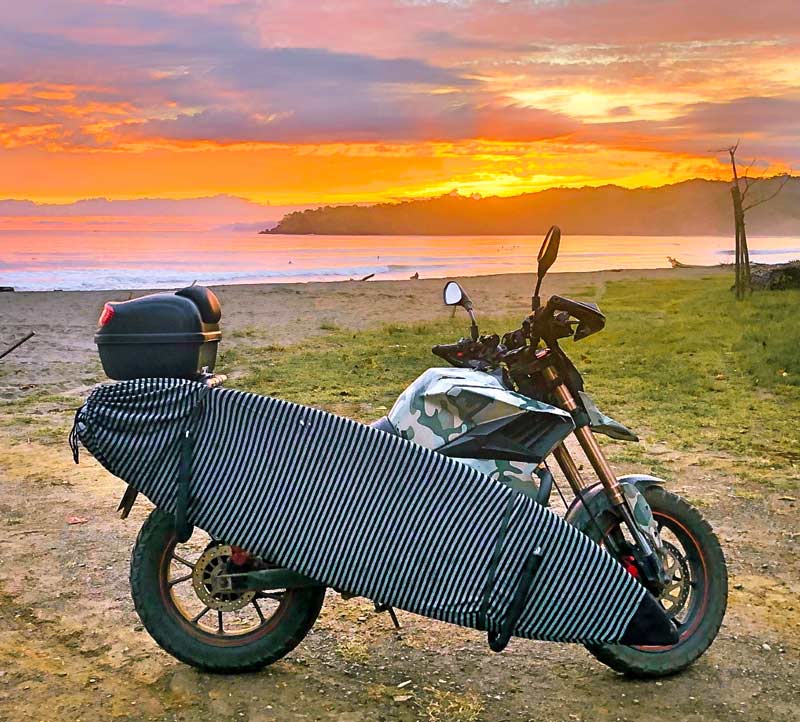 Dual-C clamp rack shown mounted to a motorcycle parked next to the beach. There is a beautiful sunset in the background, and surfers are out in the lineup.