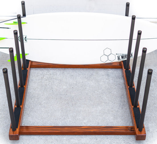 Top view of the Pig Dog Floor Rack for Surfboards & SUP in a high-gloss mahogany finish.  The board rack is holding a single white channel islands surfboard with green fins. 