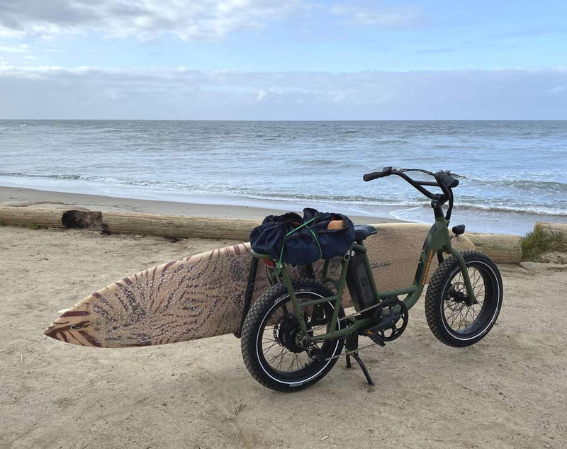 green e-bike at the beach using dual mount to hold a brown longboard checking the surf