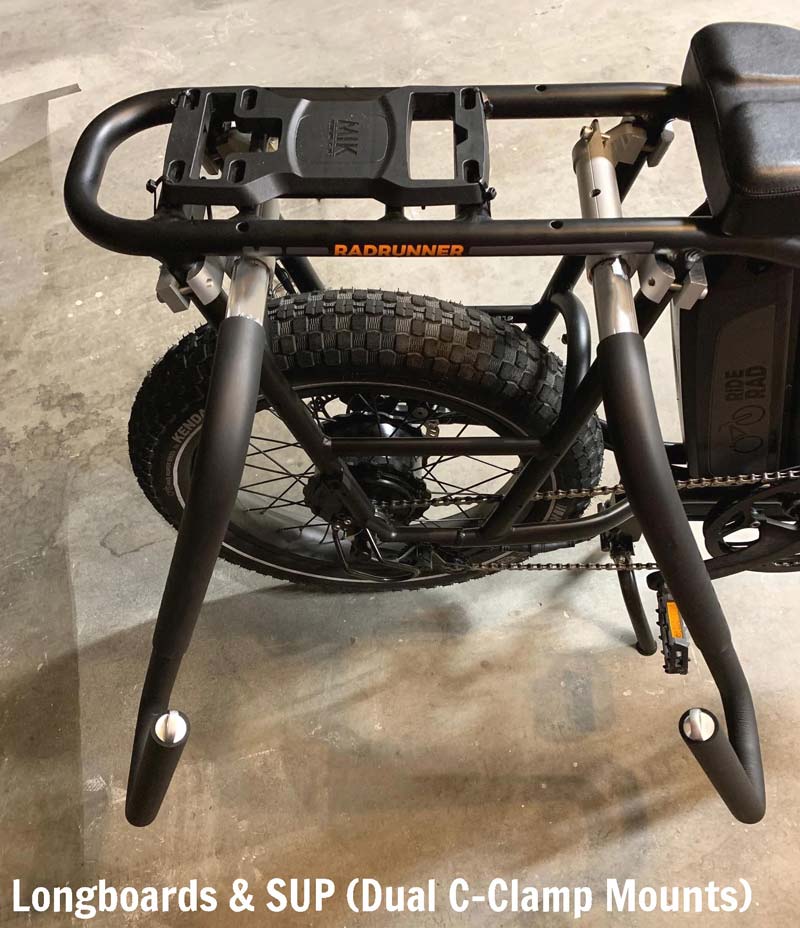 Radrunner e-bike electric bicycle with a surfboard rack mounted on the rear cargo rack.  White text reads "Longboards & SUP (Dual C-clamp Mounts)"